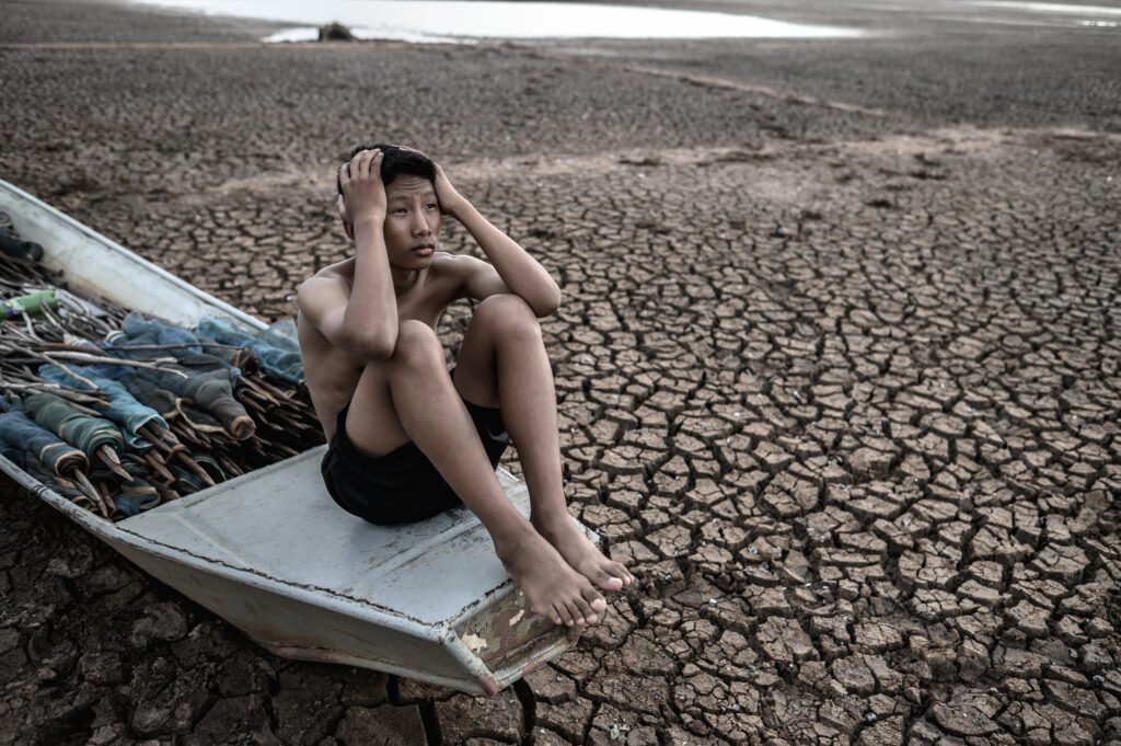 The boy sat on a fishing boat and caught his head on dry soil showing climate anxiety amid climate change