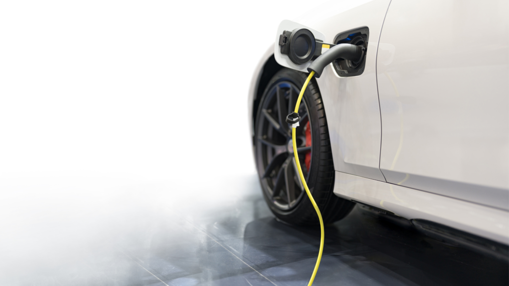 A white electric vehicle being charged, with the yellow charging cable plugged into the car's side charging port.