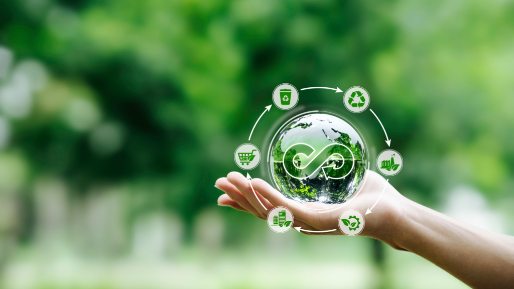 A hand holds a glass globe with a circular economy symbol, surrounded by icons representing recycling, energy, and sustainability, set against a green, blurred background.